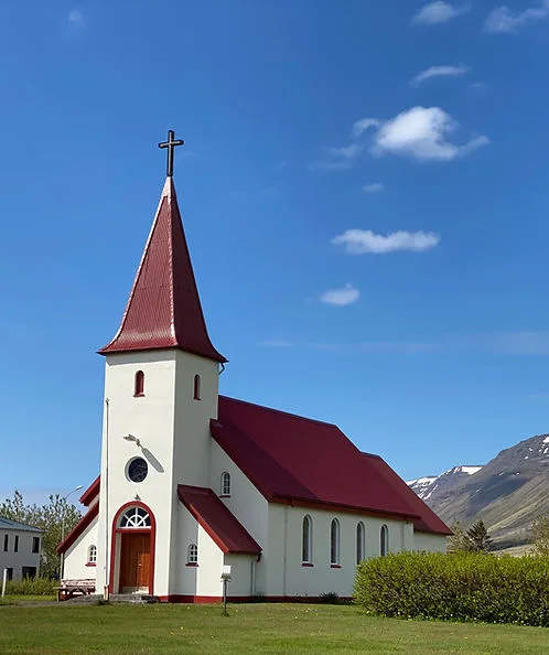 Icelandic church with red roof against a blue sky and mountains
